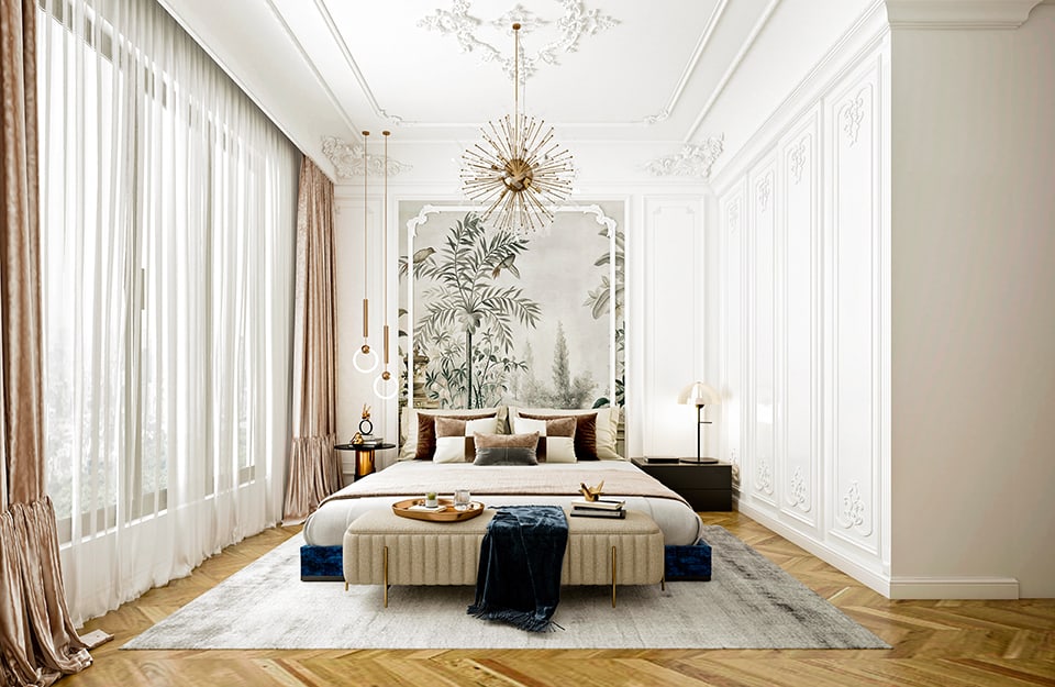 Luxurious bedroom with white framed walls, stucco ceiling and back wall with large wallpaper with a botanical-tropical theme. The large bed, in a frame covered with blue velvet, stands under a large golden globe chandelier with many rays. Two other LED lights in the shape of a round handle also descend from the ceiling. On either side of the bed are two different small tables, both black, one circular and the other rectangular, with lamps and objects on them. The bed is on top of a large grey carpet. At the end of the bed is a beige upholstered bench, echoing the blanket, and on it are books and a tray with breakfast crockery. The left wall is almost completely windowed, with white and beige satin curtains. The floor is herringbone parquet;