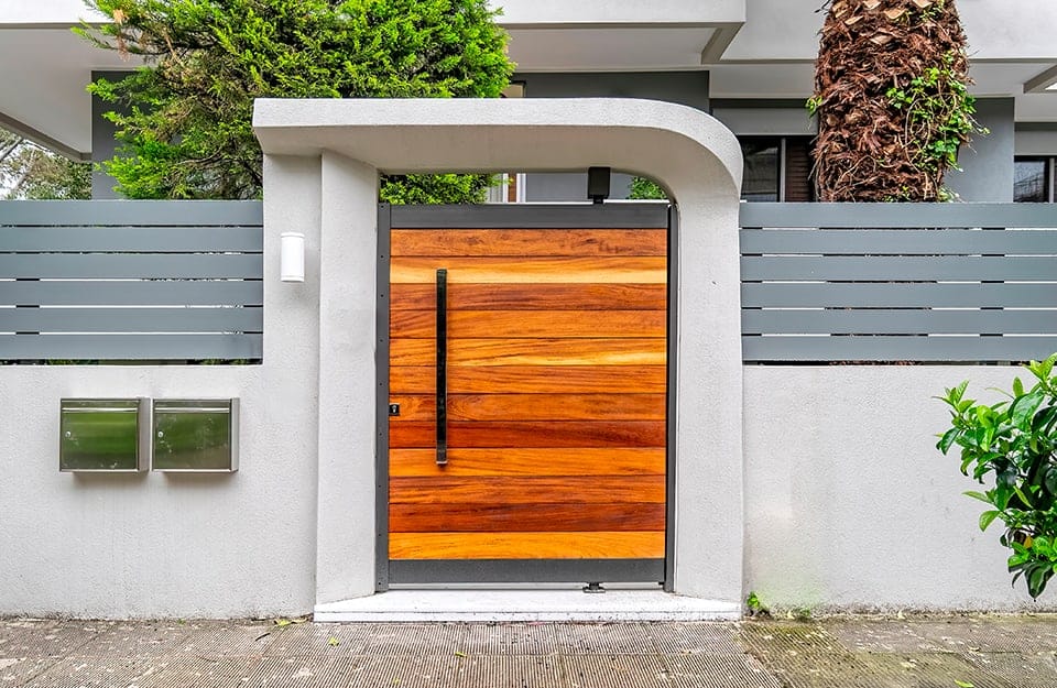 Il cancello esterno di un'abitazione moderna. La porta è in legno con assi orizzontali con venature a vista e diversi effetti cromatici