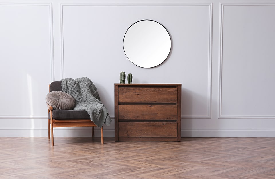 Spacious entrance hall with white wood panelling, dark wood chest of drawers, circular mirror and modernist armchair