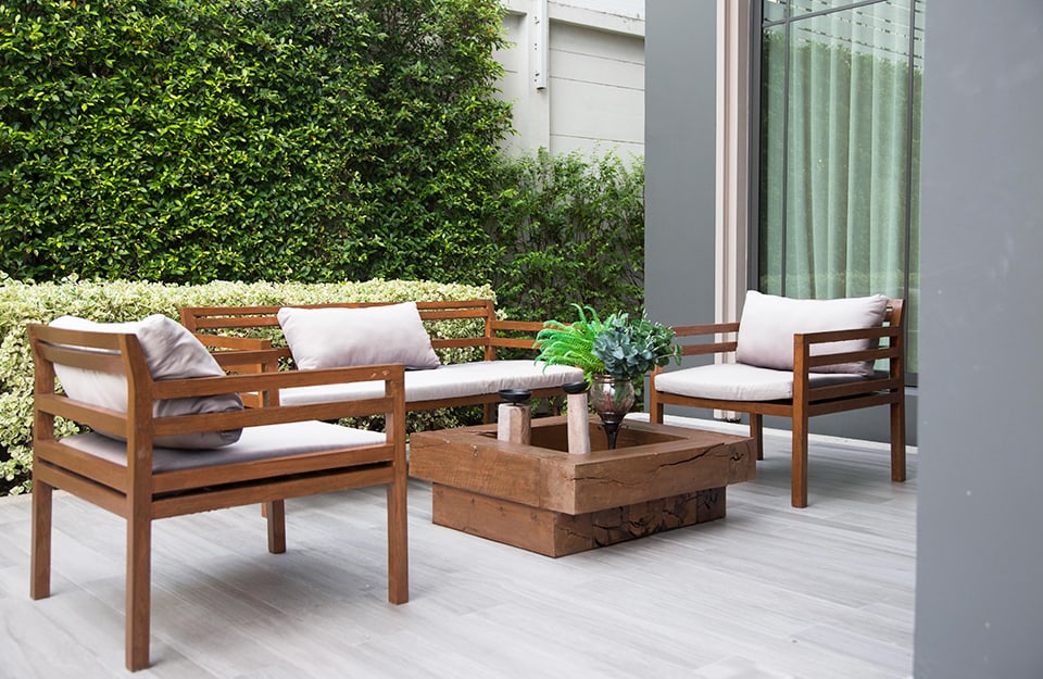 Jardín con mobiliario de estilo moderno, con sillones de madera de líneas esenciales y una gran mesa central maciza de madera bruta tratada;