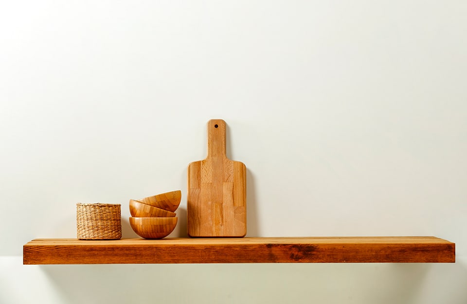 Natural wood shelf, on which a wooden chopping board and bowls and a small wicker basket rest;
