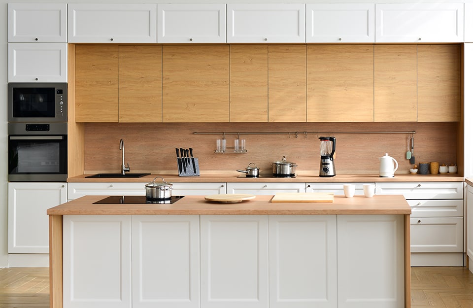 Una cocina en los colores del blanco y la madera natural, con una isla con estante de madera natural y armarios de pared con veta vista;
