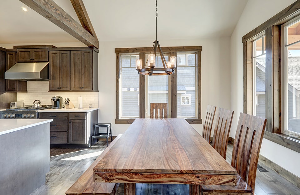 Open space con cucina e luminosa sala da pranzo in stile rustico, con lungo tavolo in legno con venature a vista, da un lato delle alte sedie dello stesso stile e dall'altro una lunga panca