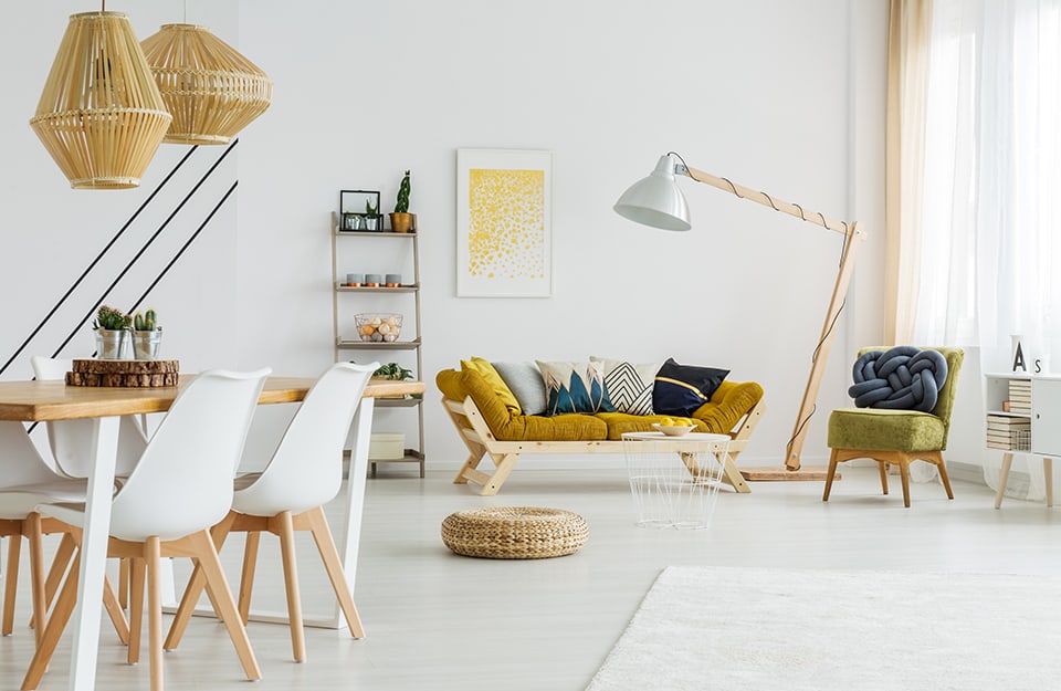 Luminoso salotto in stile scandinavo con pareti bianche e pavimento chiaro, mobili in legno naturale e divano in legno con cuscini color giallo senape