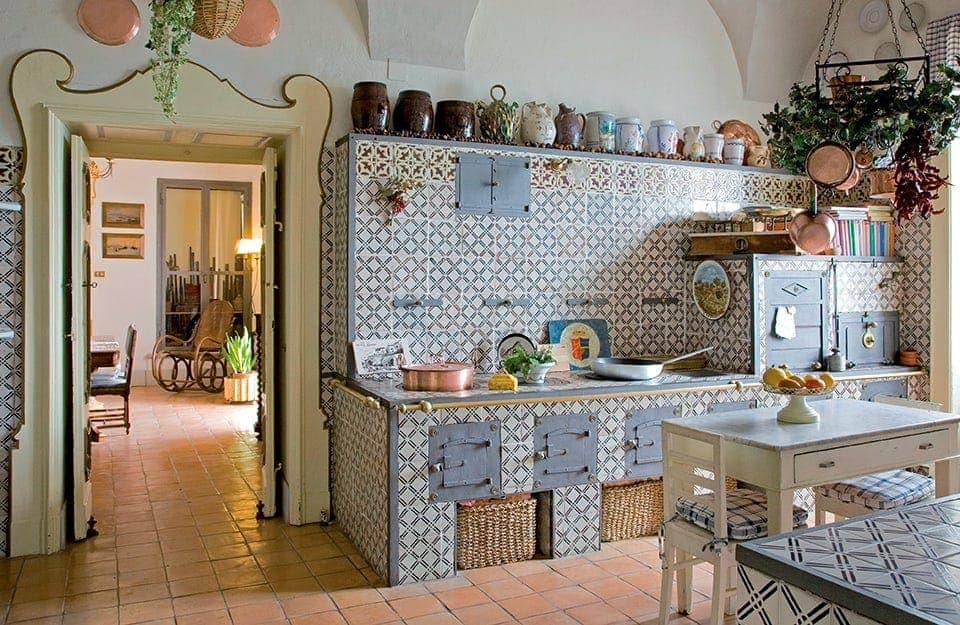 Una cucina tradizionale in stile mediterraneo, con maioliche, cesti in vimini, pentolame in rame, vasi in ceramica, poltrona in vimini, e tavolo in legno e pietra