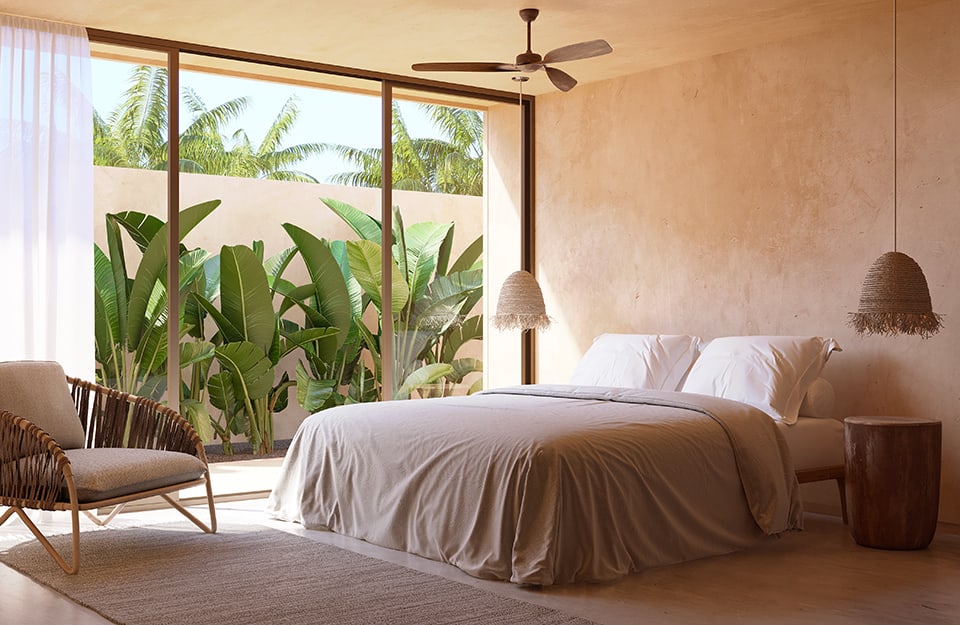 Camera da letto di una casa messicana in stile Mérida, con pareti dai colori neutri caldi, ventilatore da soffitto e grande finestrone a parete che dà su un piccolo cortile con delle palme