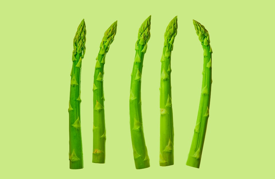 Cinque asparagi disposti parallelamente su sfondo verde chiaro