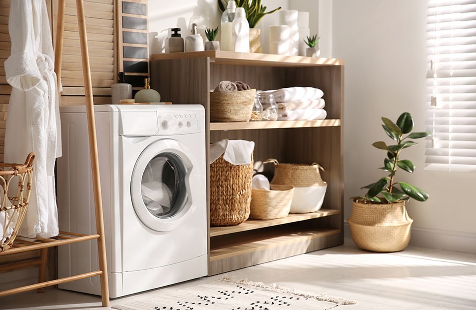 Una luminosa stanza lavanderia con una lavatrice ed arredi in legno pieni di cestini di vimini, asciugamani e piante
