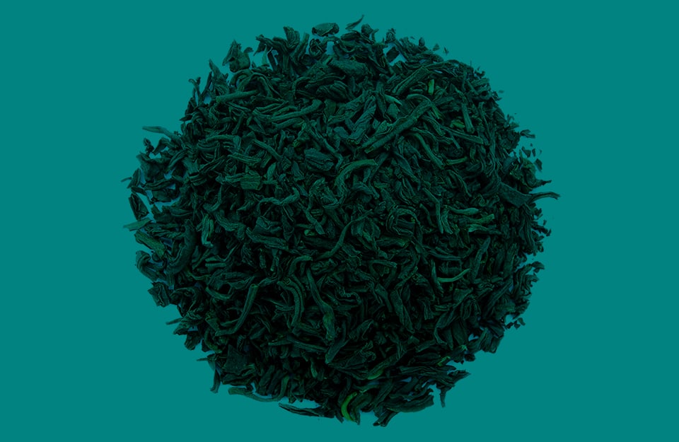 Un cerchio formato da foglie di tè essiccate su sfondo color teal, o “foglia di tè”