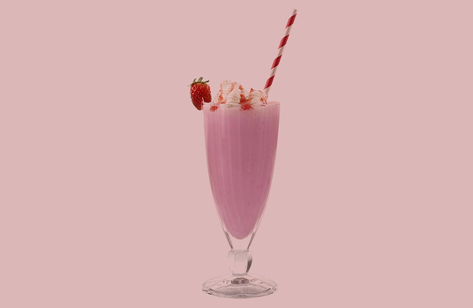 Un bicchiere di frappè alla fragola con panna, cannuccia a righe bianche e rosse e fragola decorativa, su sfondo rosa frappè