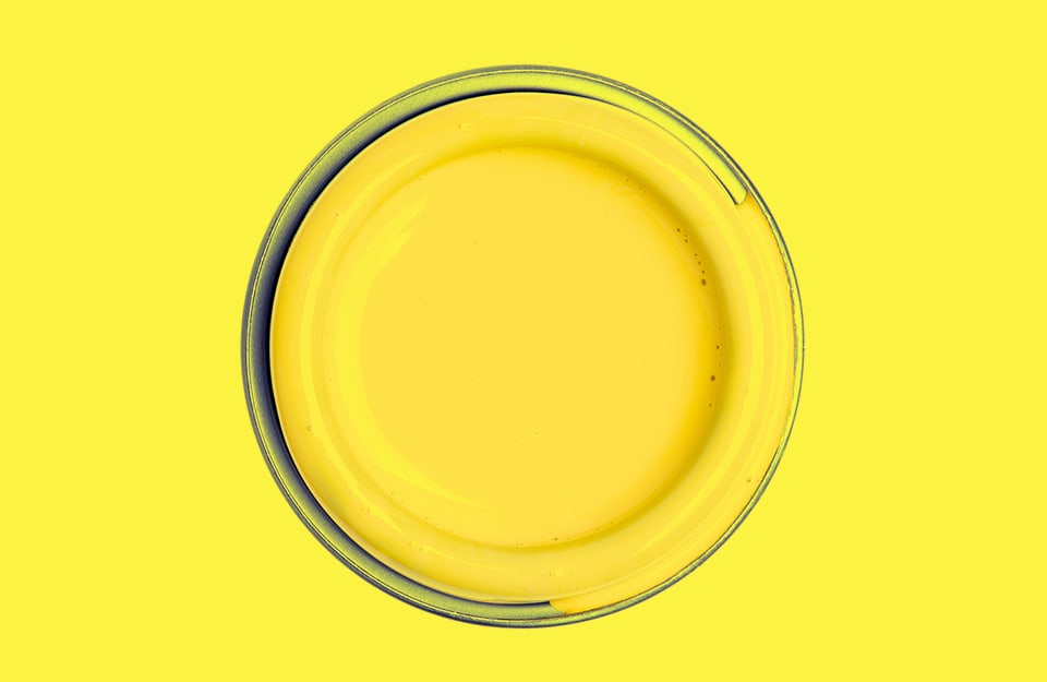 Un barattolo aperto di vernice gialla visto dall'alto, su sfondo giallo