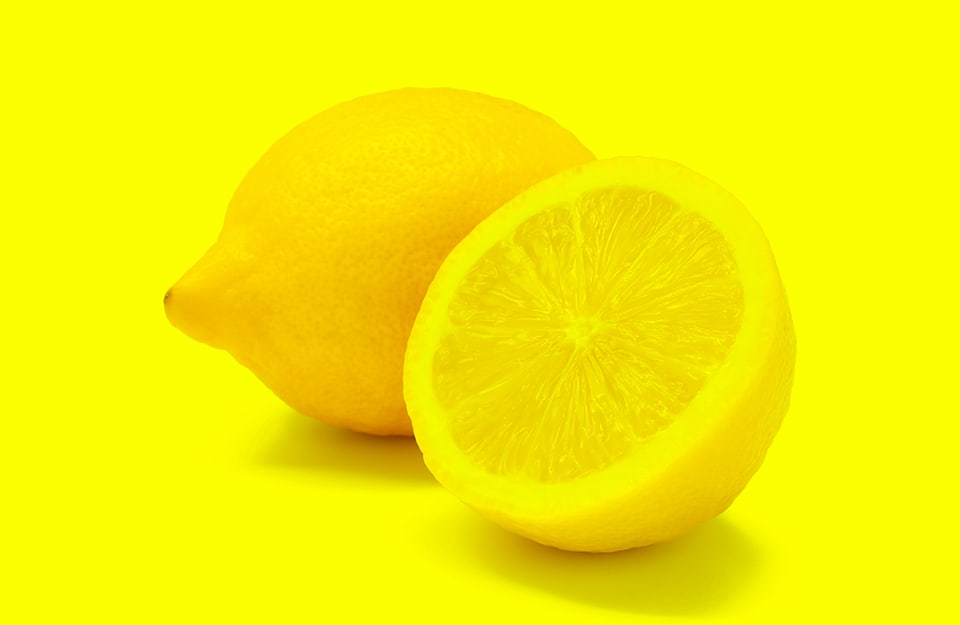 Due limoni, uno dei quali tagliato a metà, su sfondo giallo limone