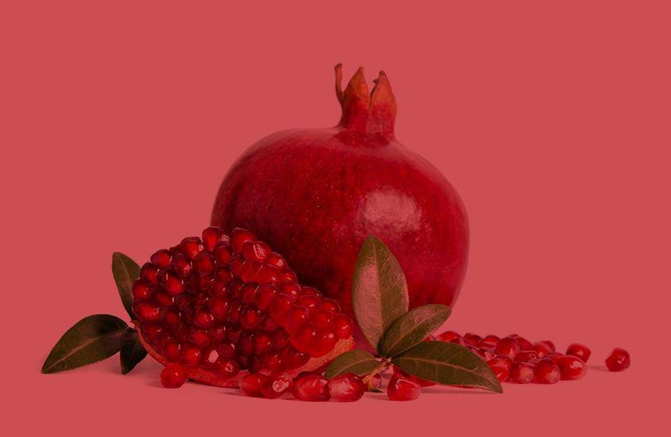 Un frutto di melograno accanto agli arilli del frutto, su sfondo color granata