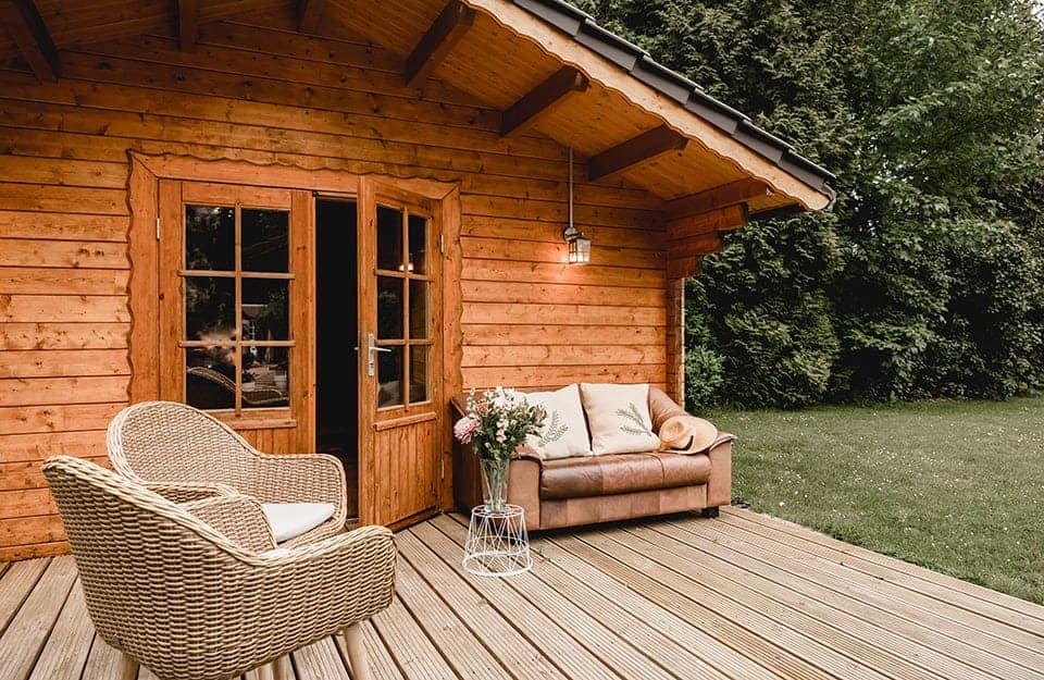 Un cottage da giardino con portafinestra, decking in legno e salotto esterno in rattan