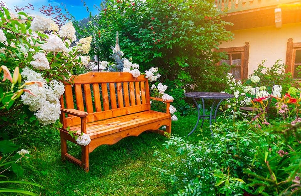 Una panchina in legno in stile rustico, ben manutenuta, in un giardino rigoglioso e pieno di fiori