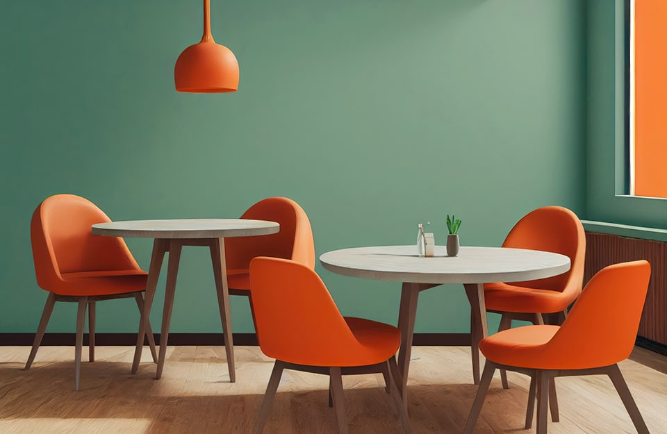 Una sala da pranzo con pareti verde salvia, tavolini in legno con pianale grigio, sedute arancioni e lampadario arancione