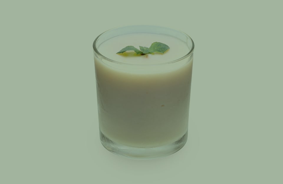 Un bicchiere di latte con dentro una foglia di menta, su sfondo color latte e menta