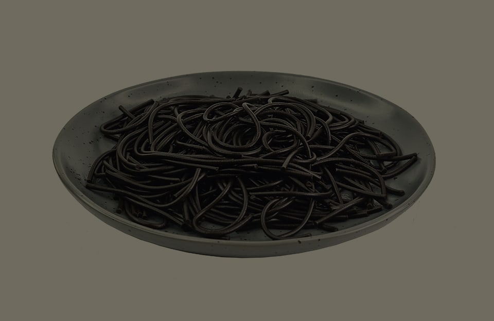 Un piatto di spaghetti al nero di seppia, su sfondo grigio