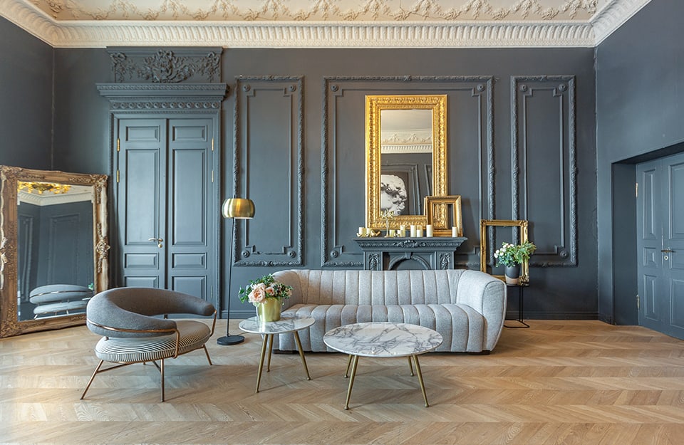 salotto chic in stile XIX secolo con mobili moderni di lusso. Le pareti sono di un blu spento e decorate con stucchi e cornici dorate. Il pavimento è in parquet