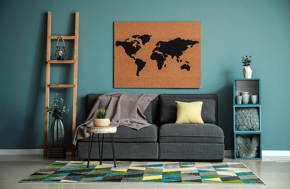 un soggiorno con pareti color ottanio, un divano grigio, una mappa sul muro, una scala pioli trasformata in portaoggetti, tappeto a motivi geometrici e scaffalino azzurro