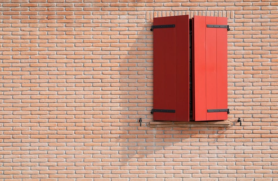 Una parete esterna a mattoncini con una finestra con scuri rosso brillante