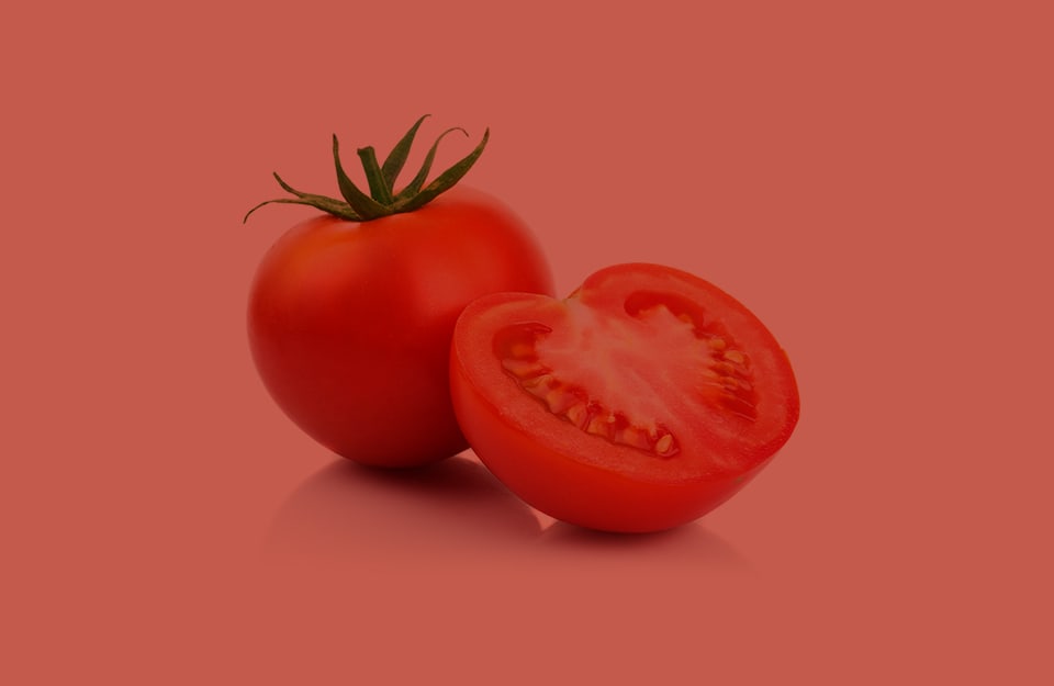 Due pomodori, uno intero e uno solo a metà, su sfondo rosso