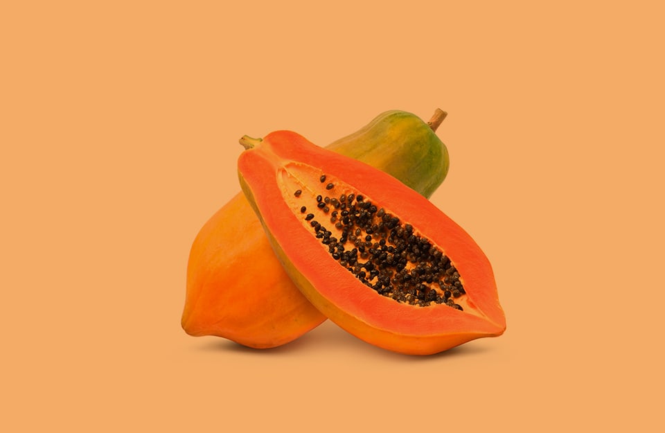 Due frutti di papaya, di cui uno solo a metà, con l'interno in vista, su sfondo color papaya