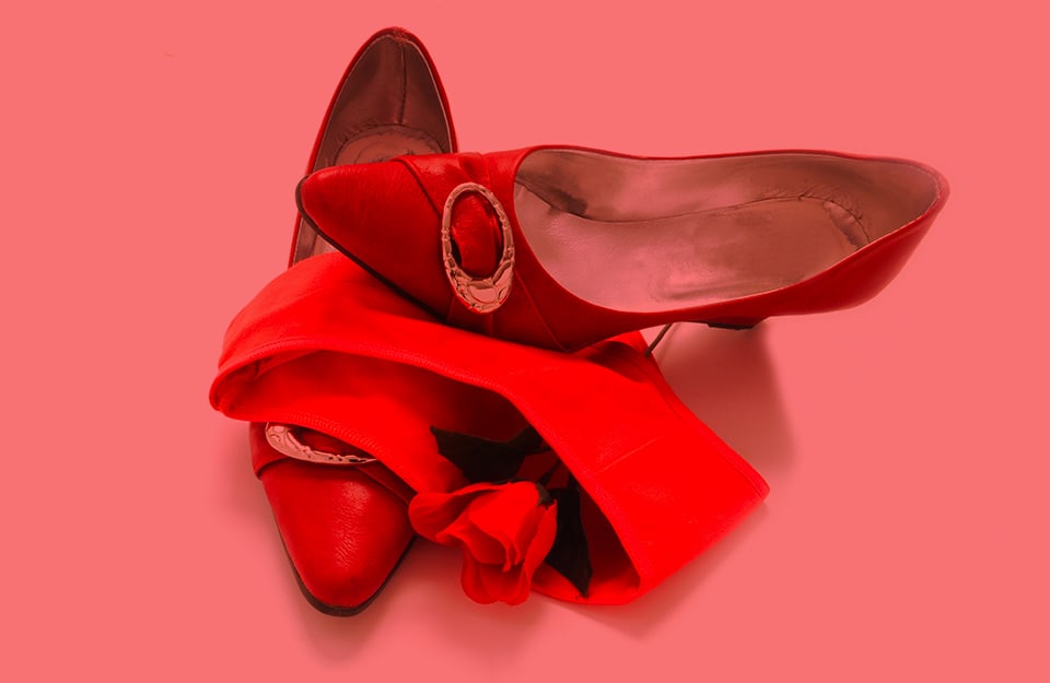 Composizione con scarpe décolleté, una rosa e un paio di mutandine, tutto in rosso, su sfondo rosso chiaro