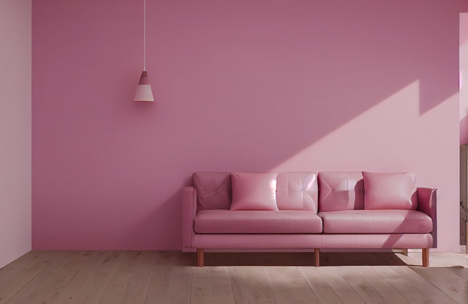 Parte di un salotto con parete rosa, divano in pelle rosa e lampada rosa che scende dal soffitto