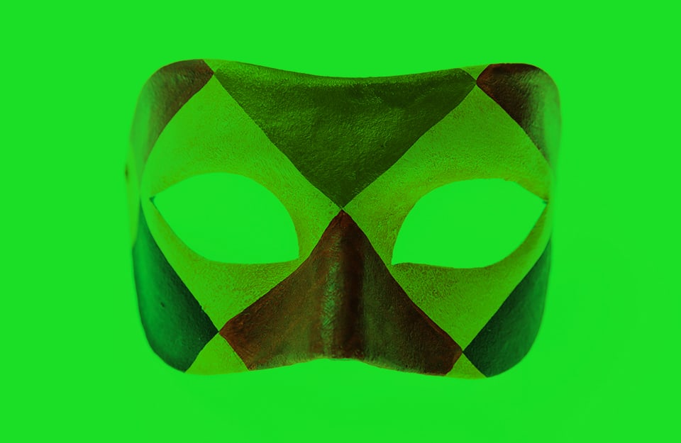 Una maschera di carnevale da viso coi colori di Arlecchino, su sfondo verde acceso