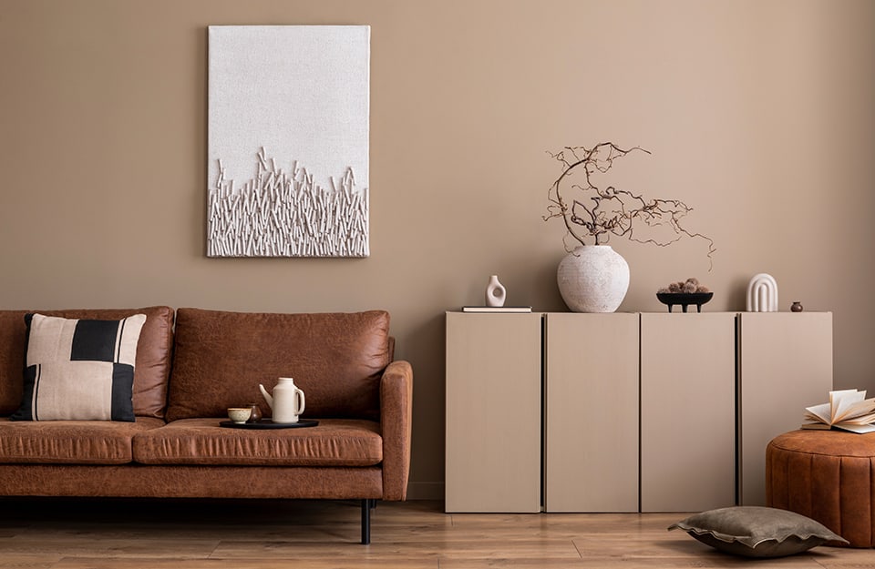 Salotto con pareti e mobile color cachi, divano in pelle marrone scura, quadro d'arte contemporanea minimale, vasi in stile giapponese e, sul sofà, un vassoio rotondo nero con tazza da tè e teiera