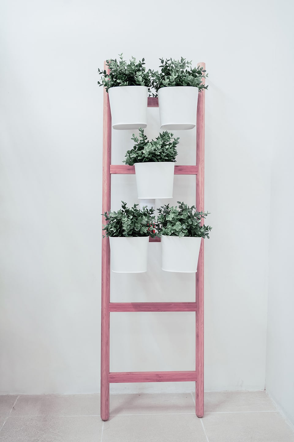 Una scala recuperata e verniciata di rosa, fissata al muro, diventa un porta piante, con piccoli vasi bianchi agganciati ai pioli