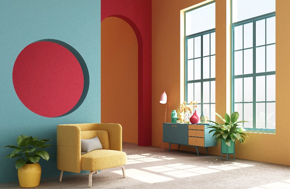 Open space moderno multicolore, con pareti in tinte diverse (azzurro, rosso e giallo), poltrona e vaso giallo, consolle azzurra e gialla, finestra interna circolare e grandi finestroni luminosi