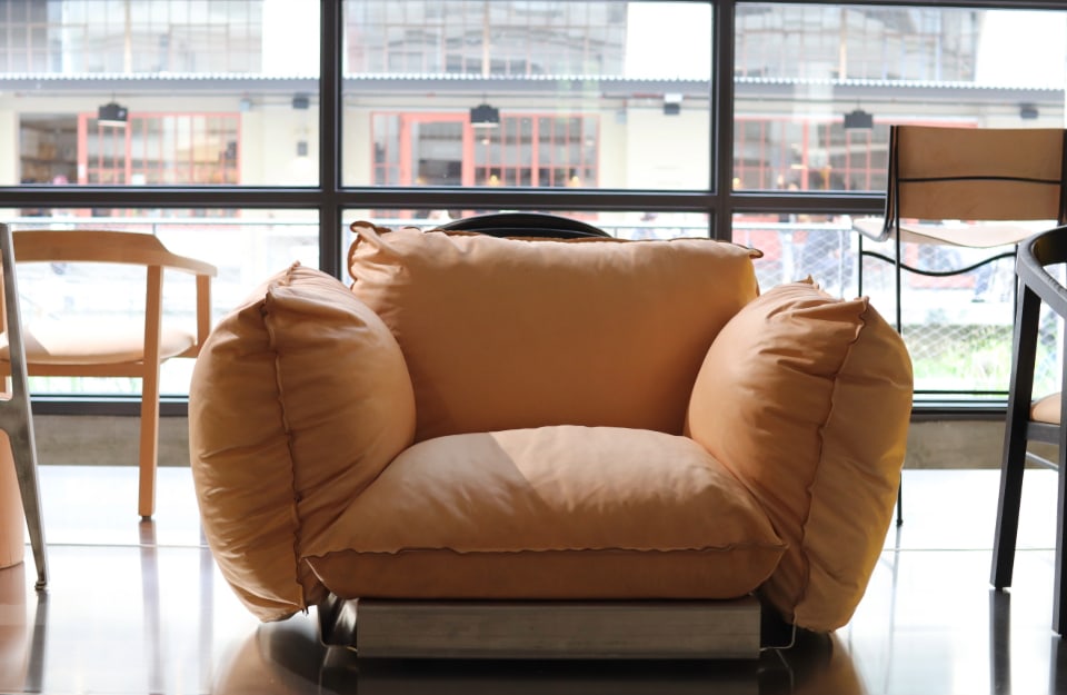 Una grande e morbida poltrona imbottita arancione foderata con materiali tecnici, con sulla sfondo altre sedie e una vetrata che si affaccia su un panorama urbano