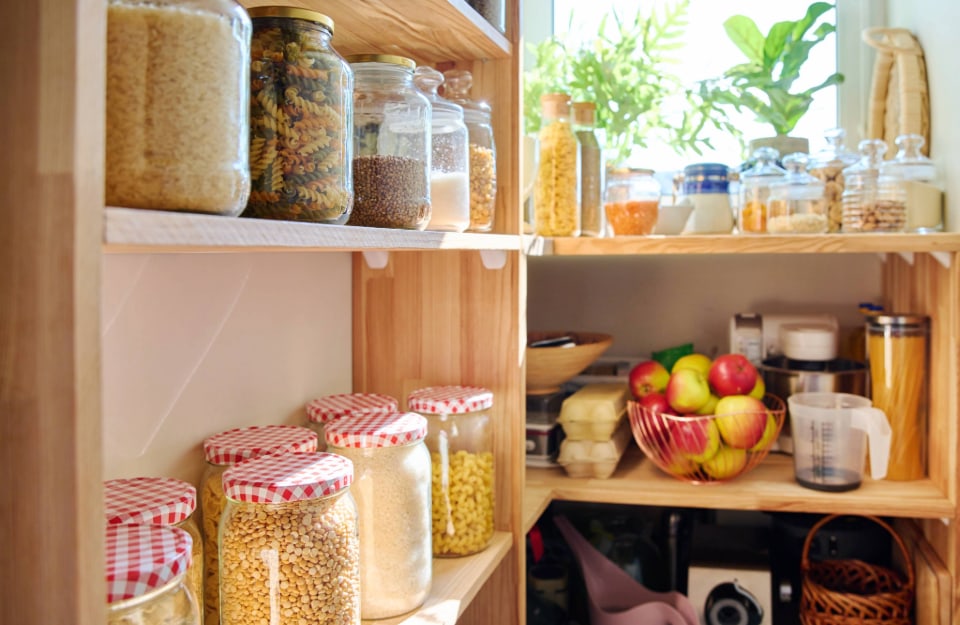 The corner of a home pantry, with shelves full of jars of pasta and pulses