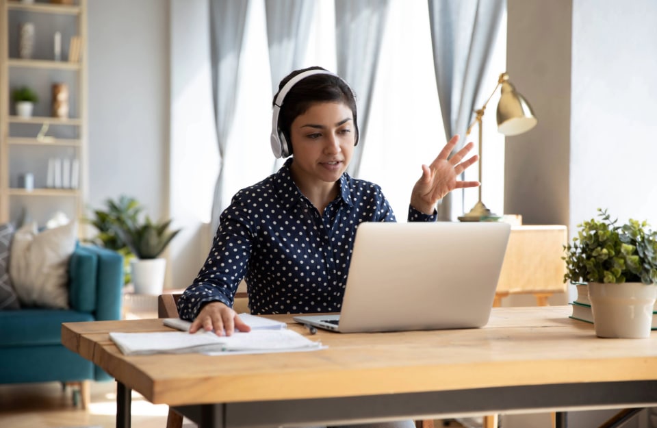 Una mujer trabaja desde casa, en el salón, en un escritorio frente a un ordenador portátil, con auriculares;