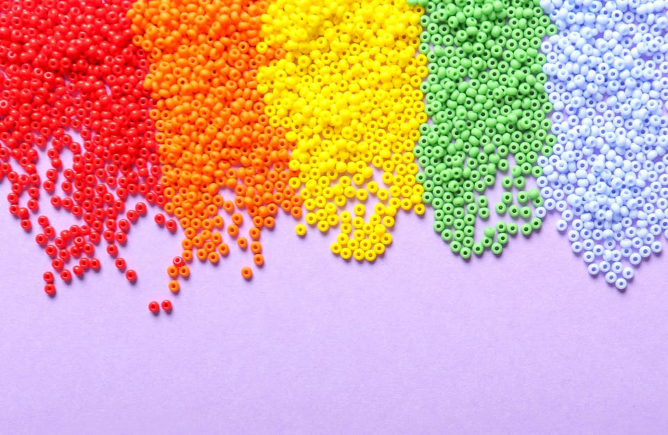 Delle perline colorate su sfondo rosa vanno a comporre alcuni dei colori dell'arcobaleno