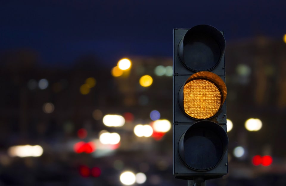 Semaforo arancione, di notte, con sulle sfondo le luci sfocate del traffico e della città