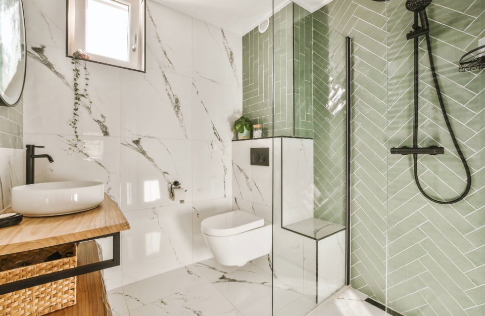 Angolo di un piccolo bagno su più livello con una parete con grandi piastrelle effetto marmo e parete doccia con piastrelle verde pastello disposte a spina di pesce