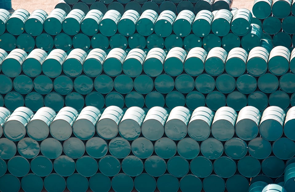 Vista dall'alto di decine di barili metallici color verde petrolio impilati in alte file