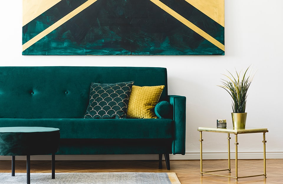 Dettaglio di un salotto con sofà in tessuto color verde petrolio, tavolino da caffè con struttura metallica, grande quadro astratto appeso alla parete bianca