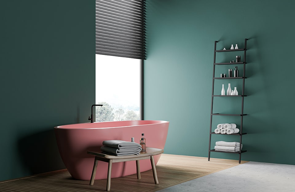 Bagno minimale con parete pitturata in color verde petrolio, porta asciugamani a scala e vasca da bagno rosa pastello dalle linee essenziali