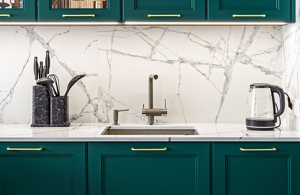 Dettaglio di una cucina con mobili in legno color verde petrolio e paraschizzi in marmo bianco