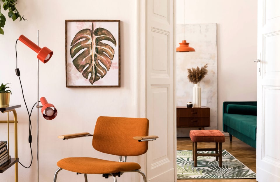 Vista su due stanze arredate in stile eclettico in una stanza con le pareti bianche e una palette anni '70 tra arredi arancioni e verdi (lampadari, sedie, divano e tappeto)