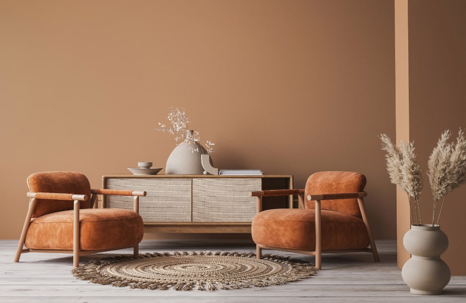 Angolo di un salotto con pareti marrone-arancio, arredi in legno naturale chiaro, poltrone arancione scuro, quasi ruggine