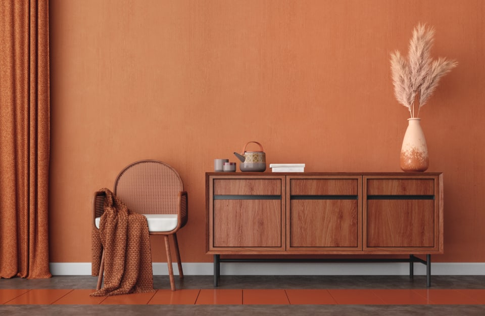 Angolo di una stanza con parete arancione scuro, consolle in legno scuro e seduta dello stesso colore