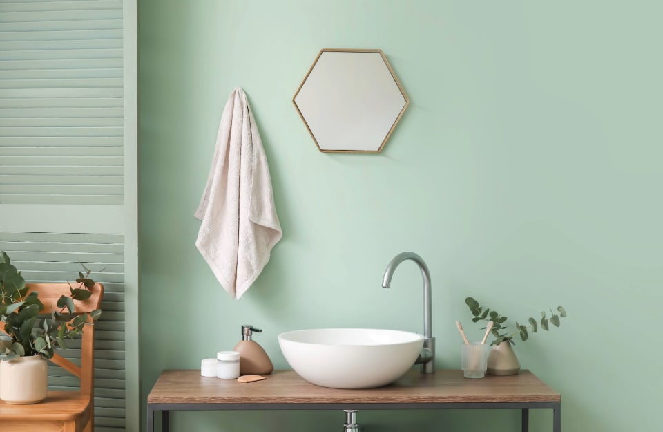 Lavandino circolare minimal in un bagno con le pareti color verde acqua, su cui sono appesi un asciugamano e un piccolo specchio esagonale