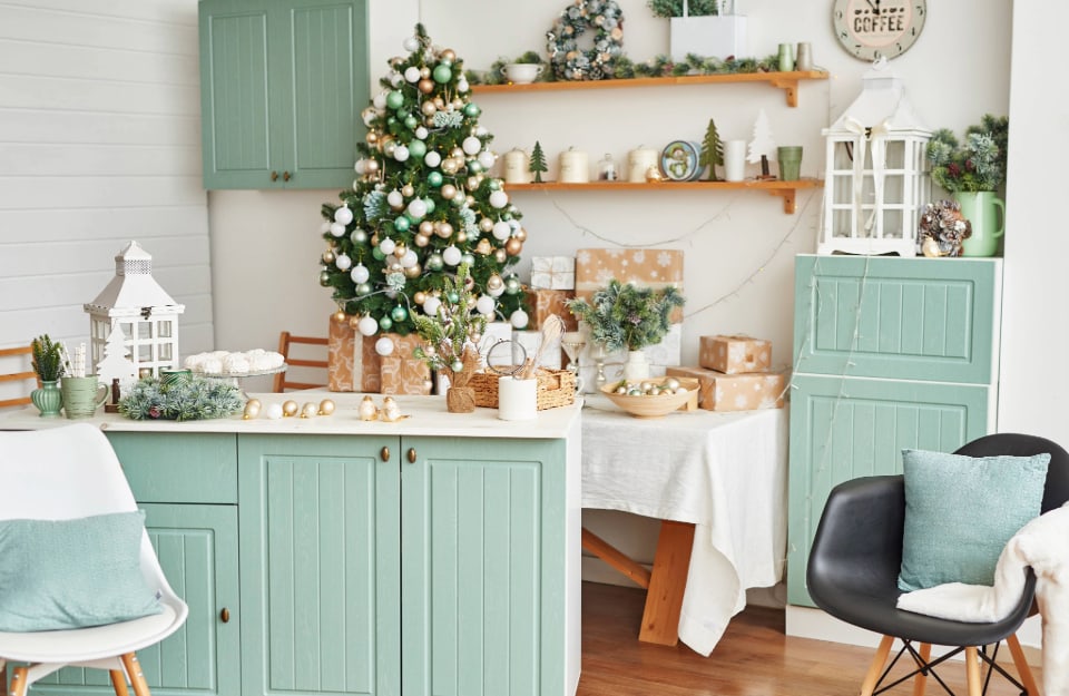 Una cucina rustica sui toni del bianco, del verde acqua e del legno naturale, con decorazioni natalizie e molte mensole