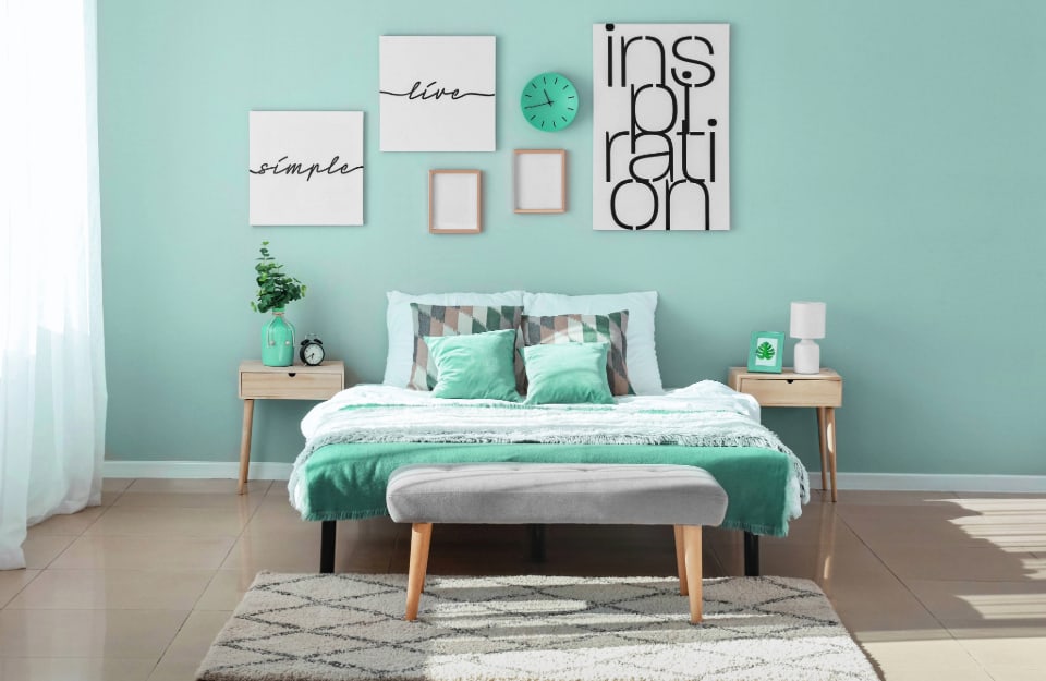 Camera da letto moderna con mobili in legno in stile scandinavo, parete verde acqua e cuscini e copriletto dello stesso colore. Sulla parete ci sono diversi quadri e poster