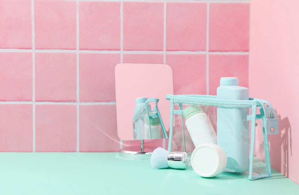 Dettaglio di un bagno, con superficie color verde acqua, flaconi dello stesso colore e piastrelle quadrate rosa pastello